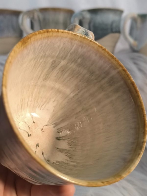 Close-up of a handmade ceramic coffee mug featuring a smooth white glaze with a light brown rim, creating a warm, cosy look